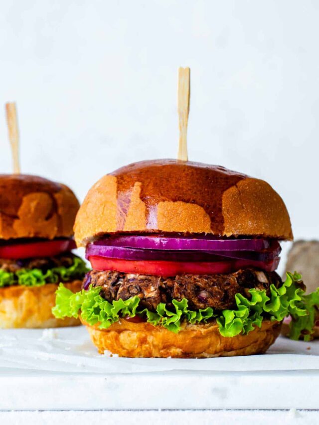 A jackfruit burger with a wooden food pick inserted in it. The burger is placed on a marble board.