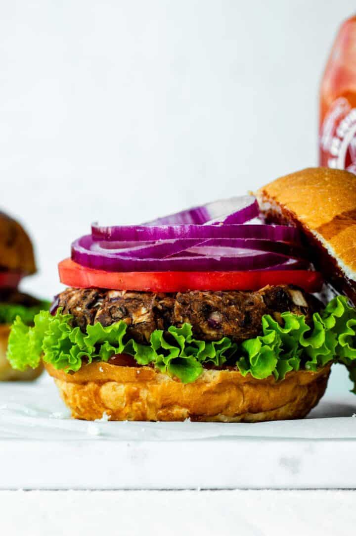 An open jackfruit burger with lettuce, patty, tomatoes, and red onion.