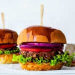 A jackfruit burger with a wooden food pick inserted in it. The burger is placed on a marble board.