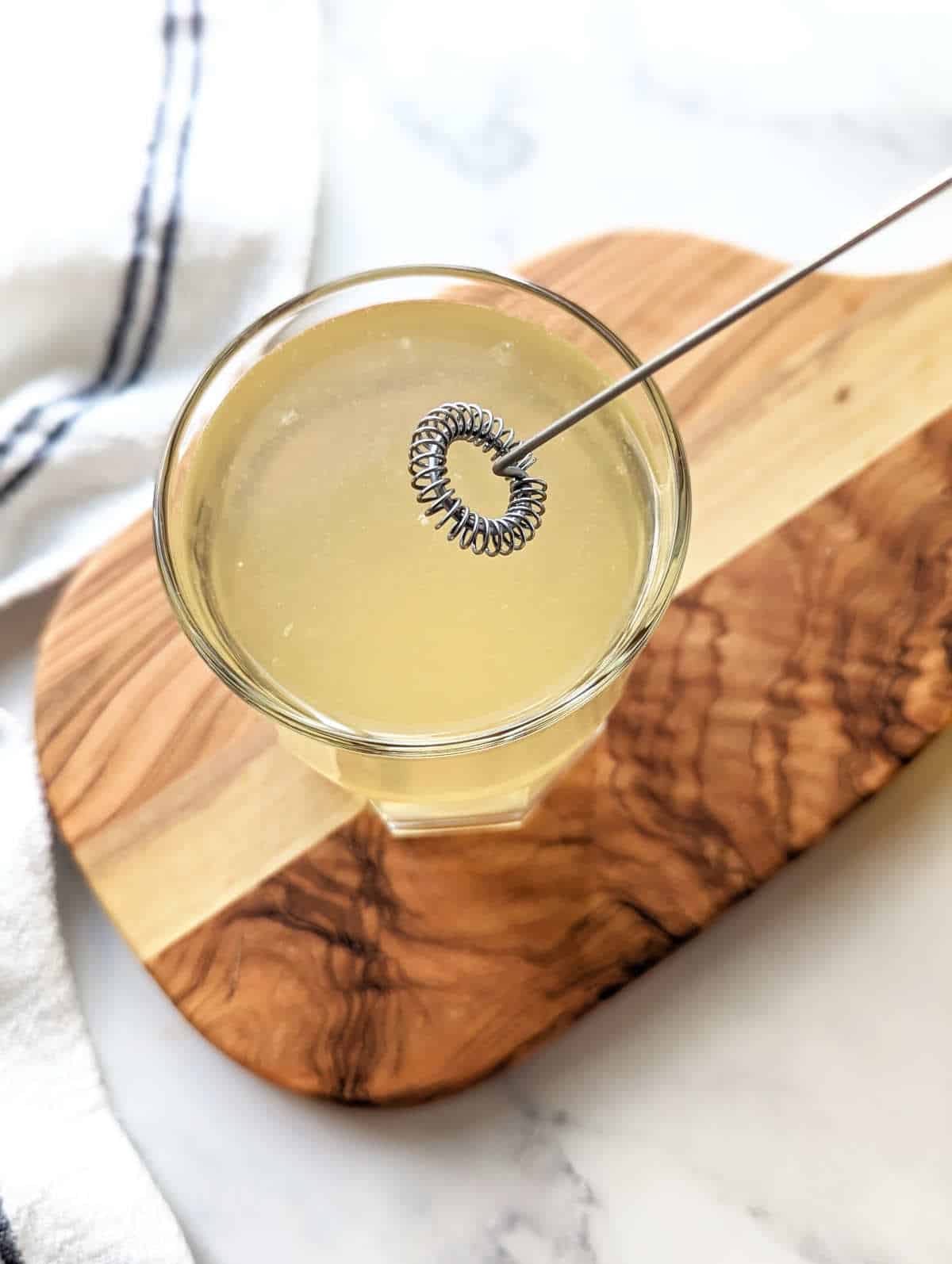 A milk frother hovering over the apple cider and vinegar and lemon juice in a glass.