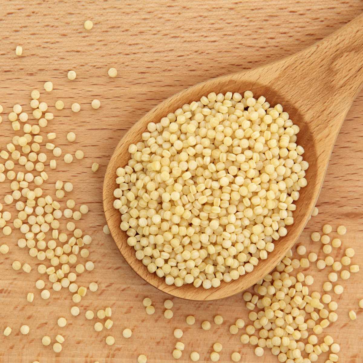 Wooden spoon holding dry pearl couscous.