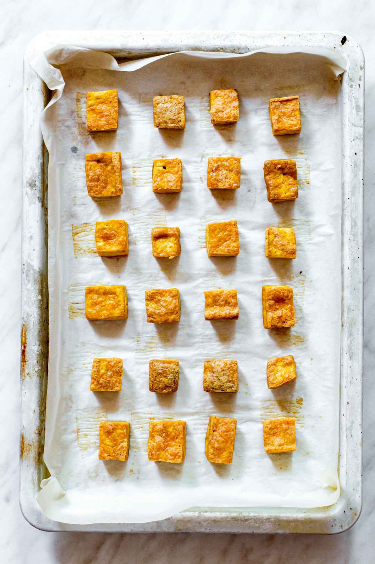 Baked tofu cubes on a baking sheet layered with parchment paper.