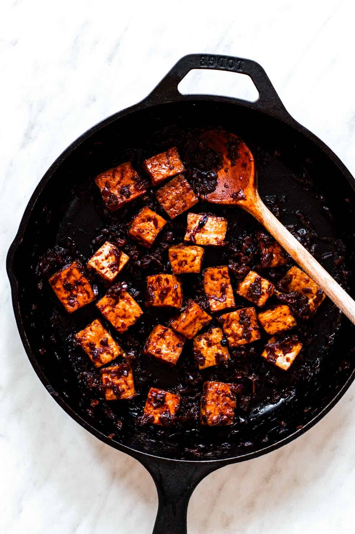 Cooking baked tofu cubes in adobo sauce in a cast-iron skillet.
