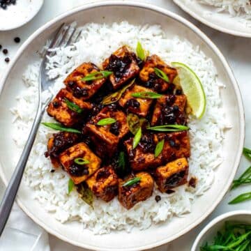 Tofu adobo served over a bed of rice and topped with sliced green onion.