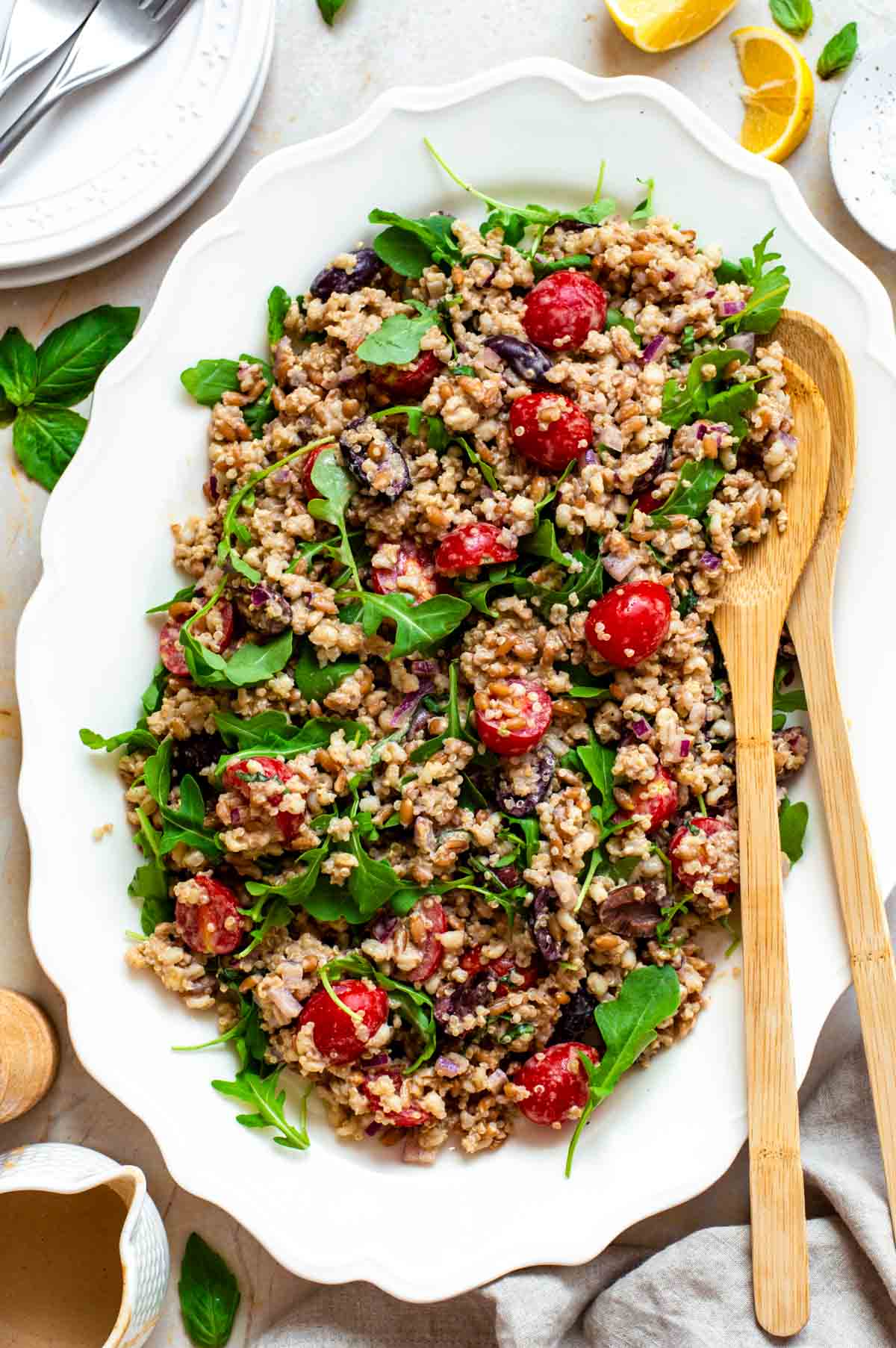 Ancient grains salad served on a white platter with wooden salad servers placed in the right corner.