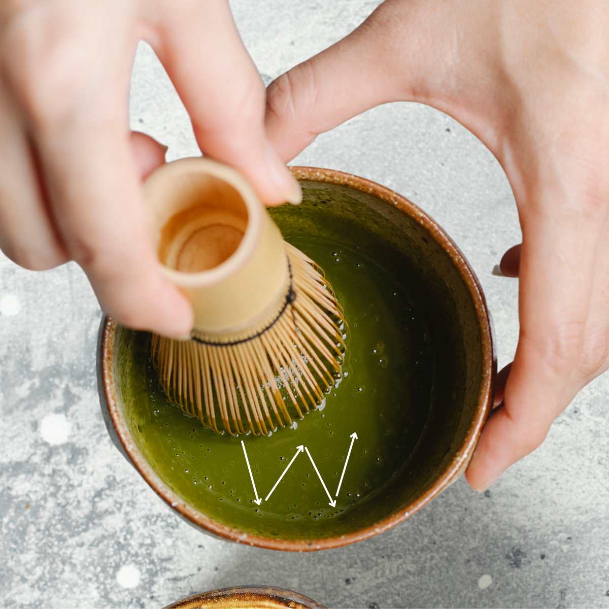 Matcha being mixed in a small bowl with arrows showing the "W" pattern for whisking.