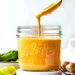 Spicy cashew dressing in a mason jar with a spoon dripping some dressing back into the jar.