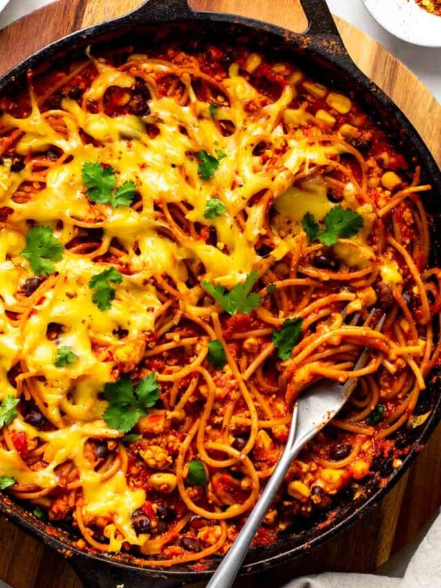 Large skillet filled with Mexican spaghetti, topped with melted dairy-free cheese and cilantro leaves.