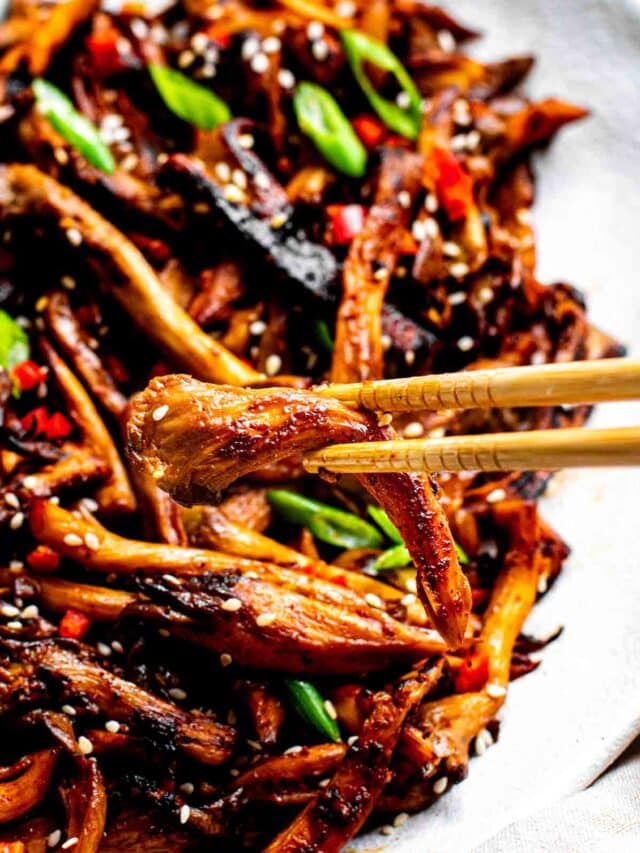 A chopstick picking up a slice of vegan bulgogi mushroom off a platter.