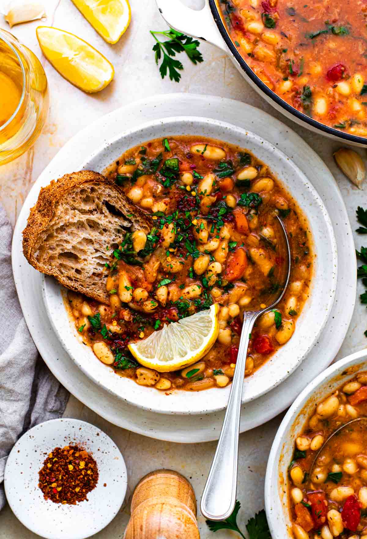 Navy bean vegetable soup served in a white bowl with a slices of sourdough bread dipped in it.