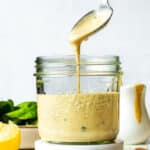 A spoon dripping tahini Caesar dressing into a glass jar.