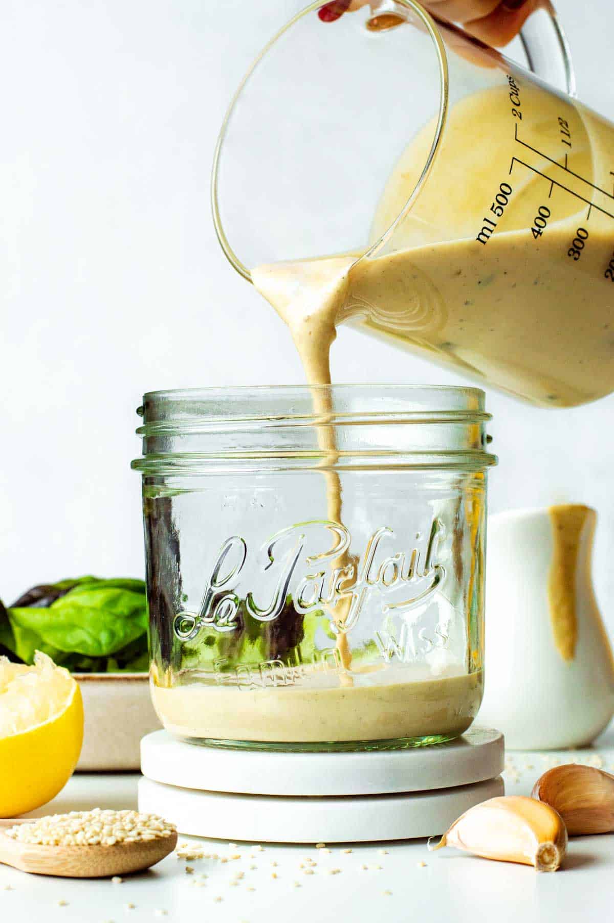 Pouring the tahini caesar dressing into a glass jar.