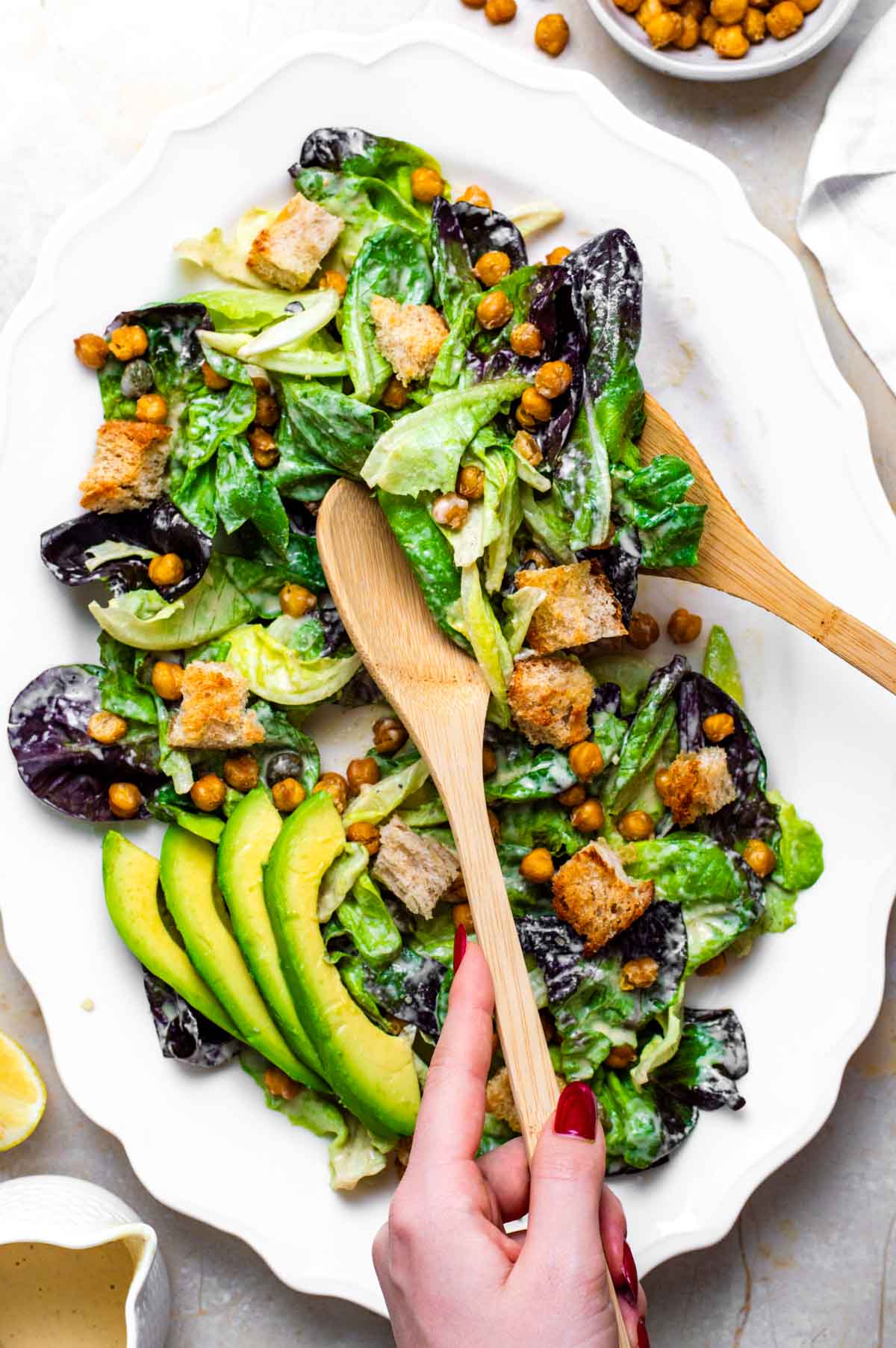 A vegan Caesar salad on a plate, made with lettuce, chickpeas, croutons, avocado slices, and the tahini caesar dressing.