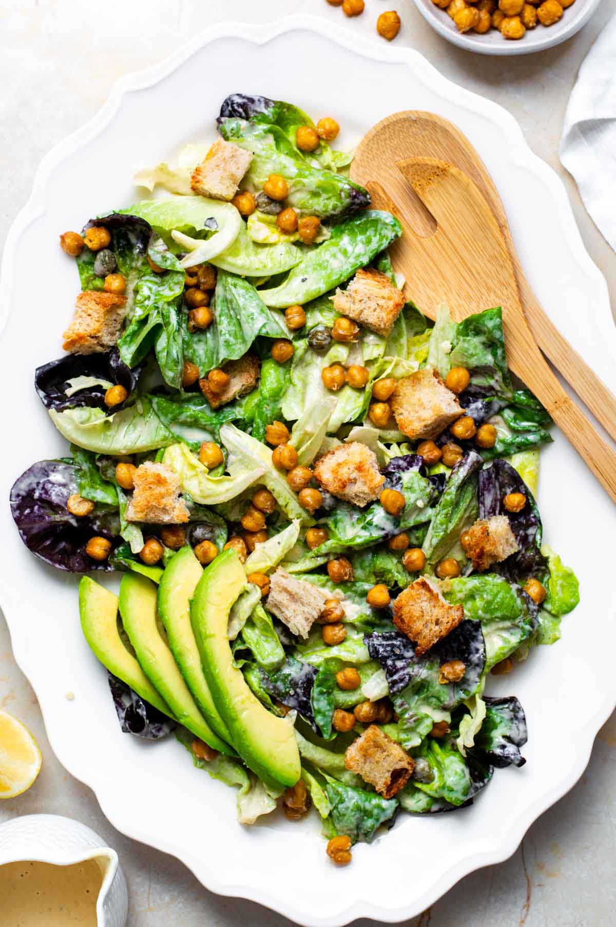 A vegan Caesar salad on a plate, made with lettuce, chickpeas, croutons, avocado slices, and the tahini caesar dressing.