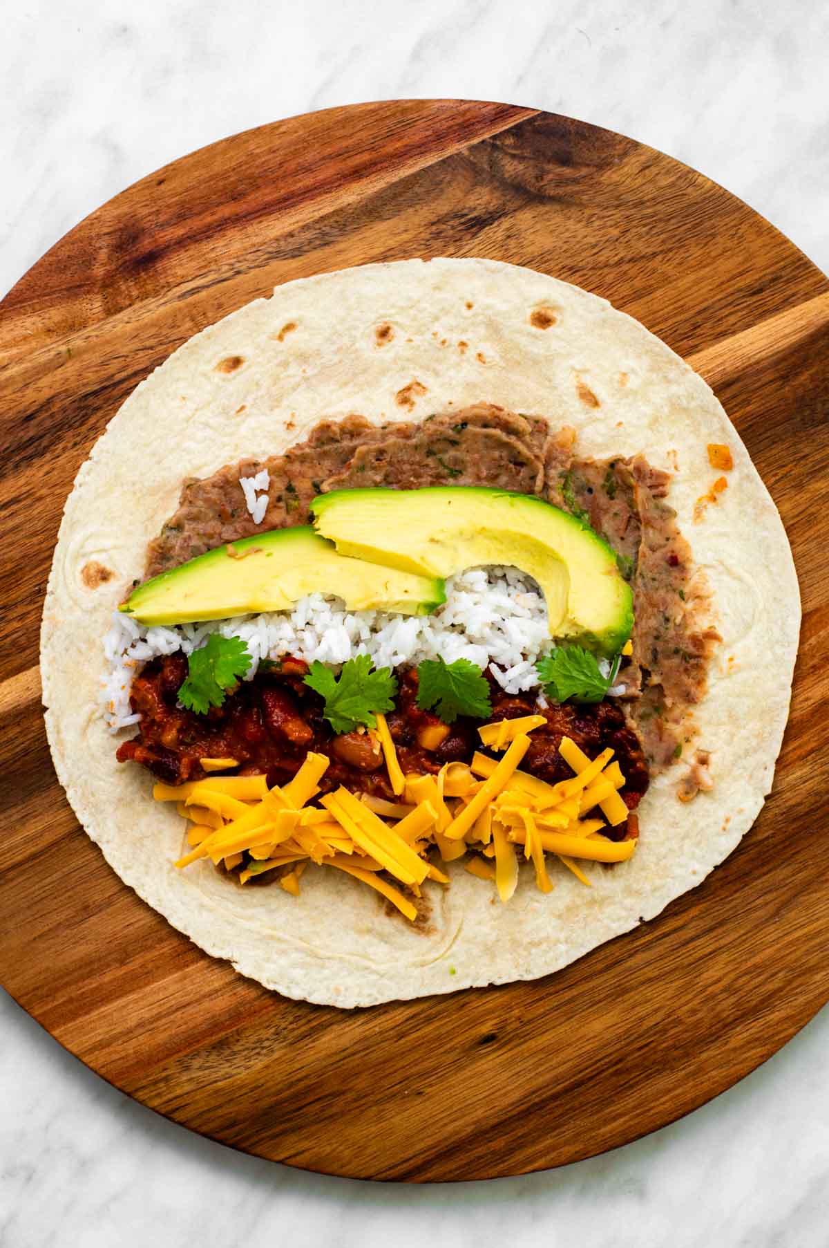 The tortilla topped with refried beans, chili, cheese, avocado, rice, and cilantro.