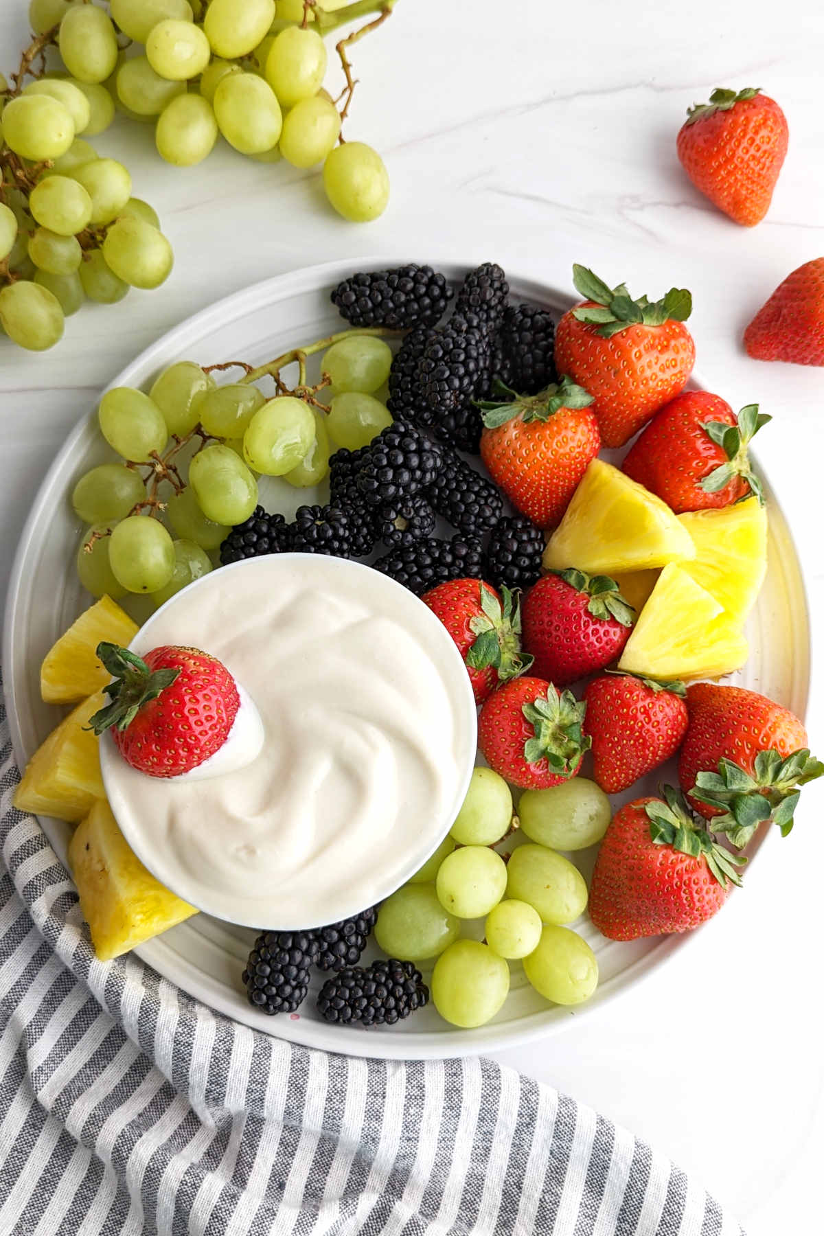 A fruit platter with various fruits and served with vegan fruit dip.