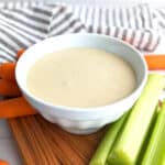 A small bowl of dijonnaise next to celery and carrots.