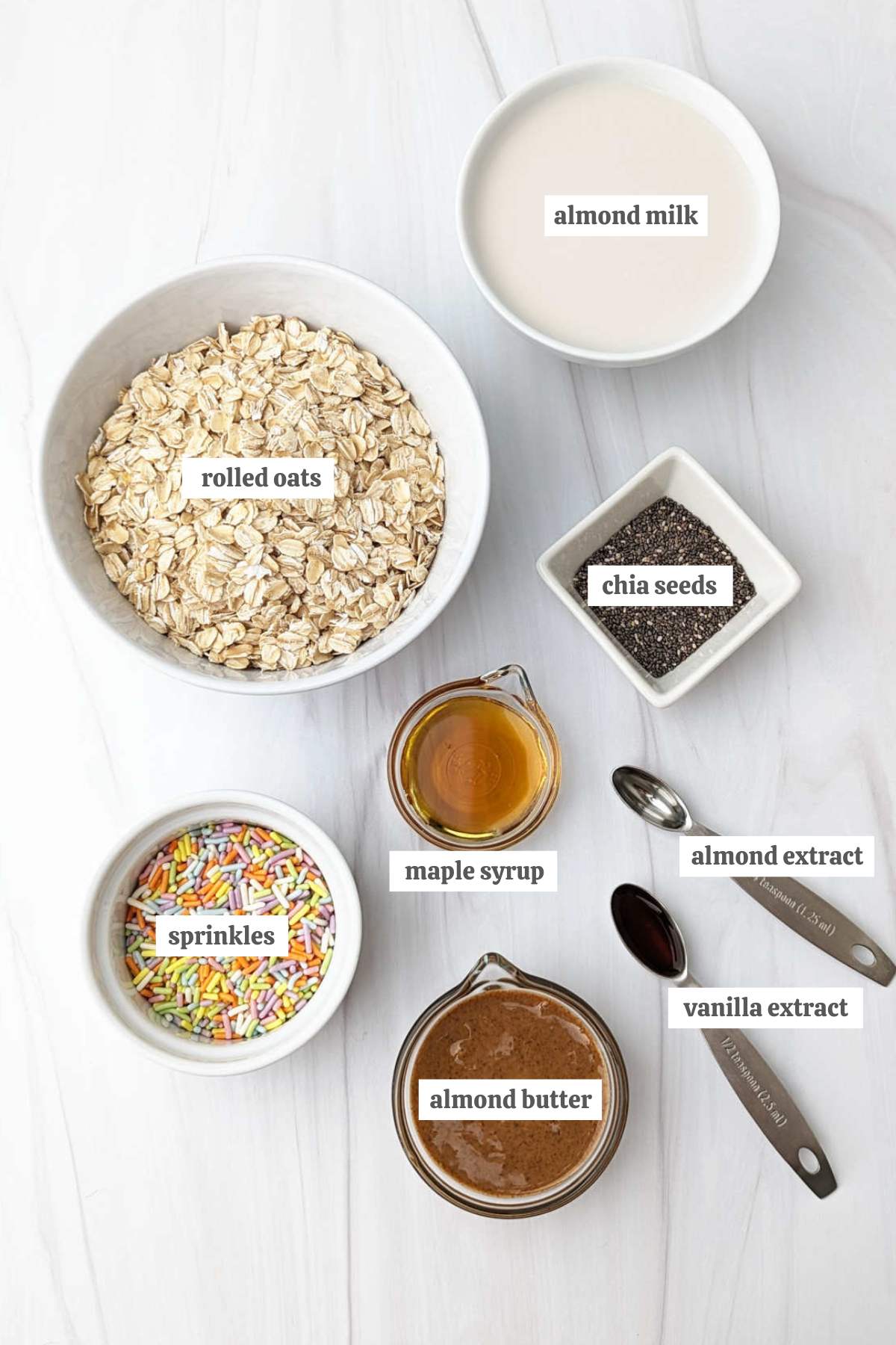 Gathered ingredients for these birthday cake overnight oats in individual bowls with labels.