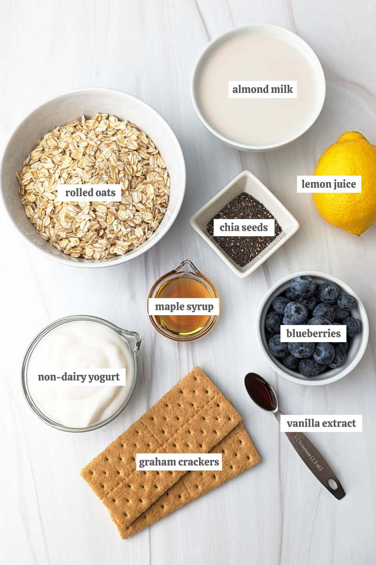 Gathered ingredients for this blueberry cheesecake overnight oats recipe in various bowls with labels.