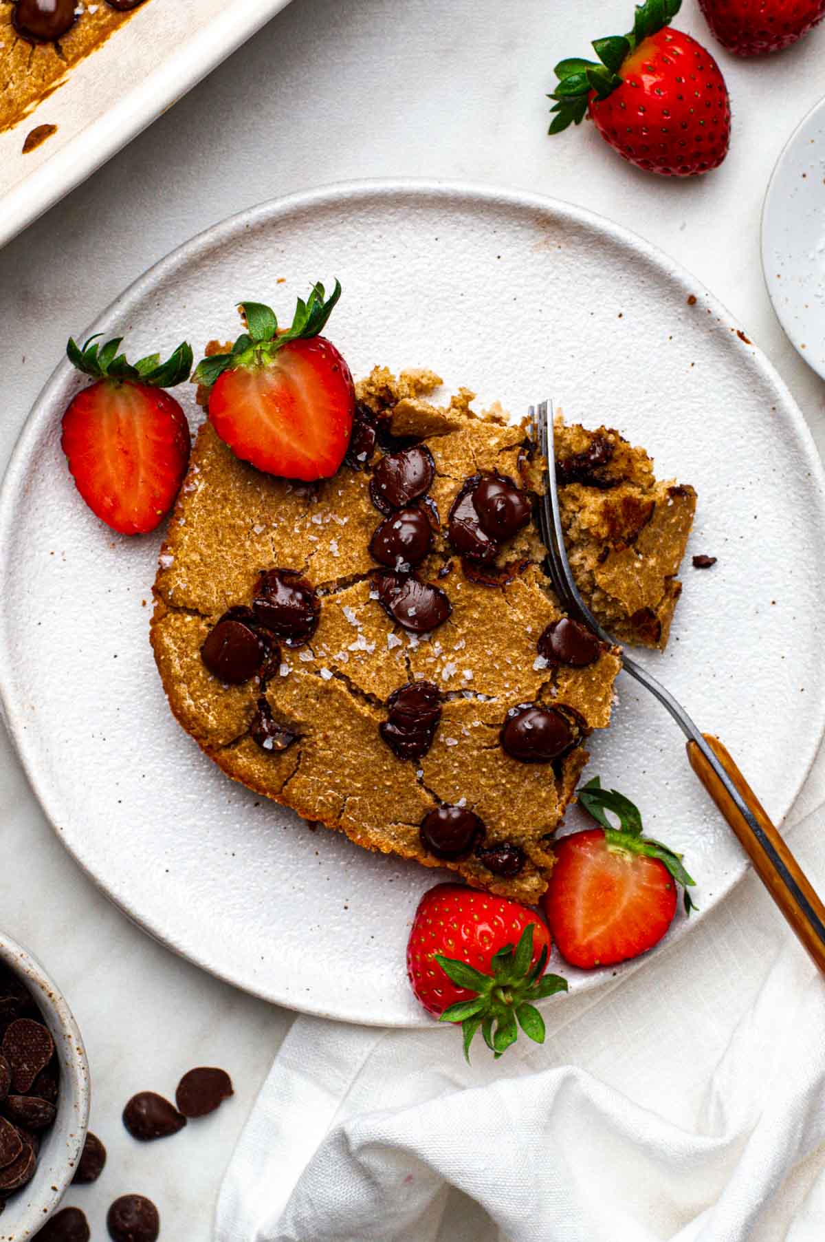 A slice of no banana baked oats on a plate with chocolate chips and sliced strawberries.