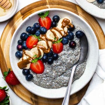 A bowl of warm chia pudding topped with fresh berries, sliced banana, and a drizzle of peanut butter.