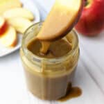 Tahini caramel dripping off an apple slice over a jar of the tahini caramel sauce.