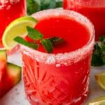 Watermelon water in a glass with a salted rim, garnished with fresh mint leaves and a slice of lime.