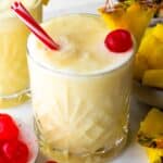 Pina colada mocktail in a glass, served with a straw and a cherry.