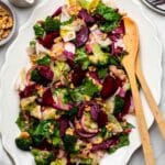A serving platter of pickled beet salad with wooden serving utensils.