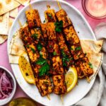 Tofu souvlaki skewers served on a white plate and topped with chopped parsley.