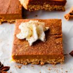 A vegan pie bar slice topped with vegan whipped cream and a dusting of ground cinnamon.