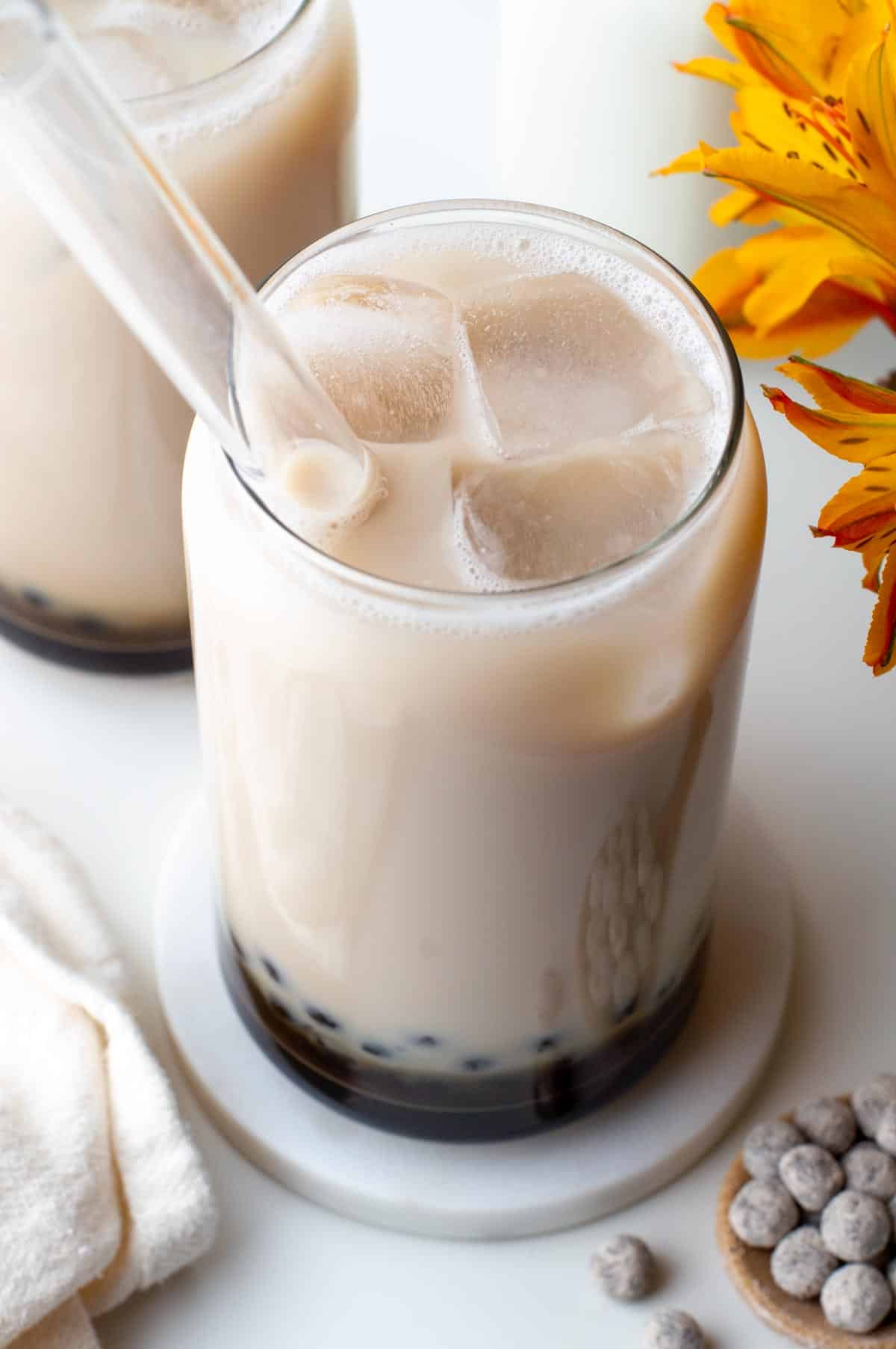 A glass of jasmine green milk tea with boba pearls in the bottom and filled with ice.