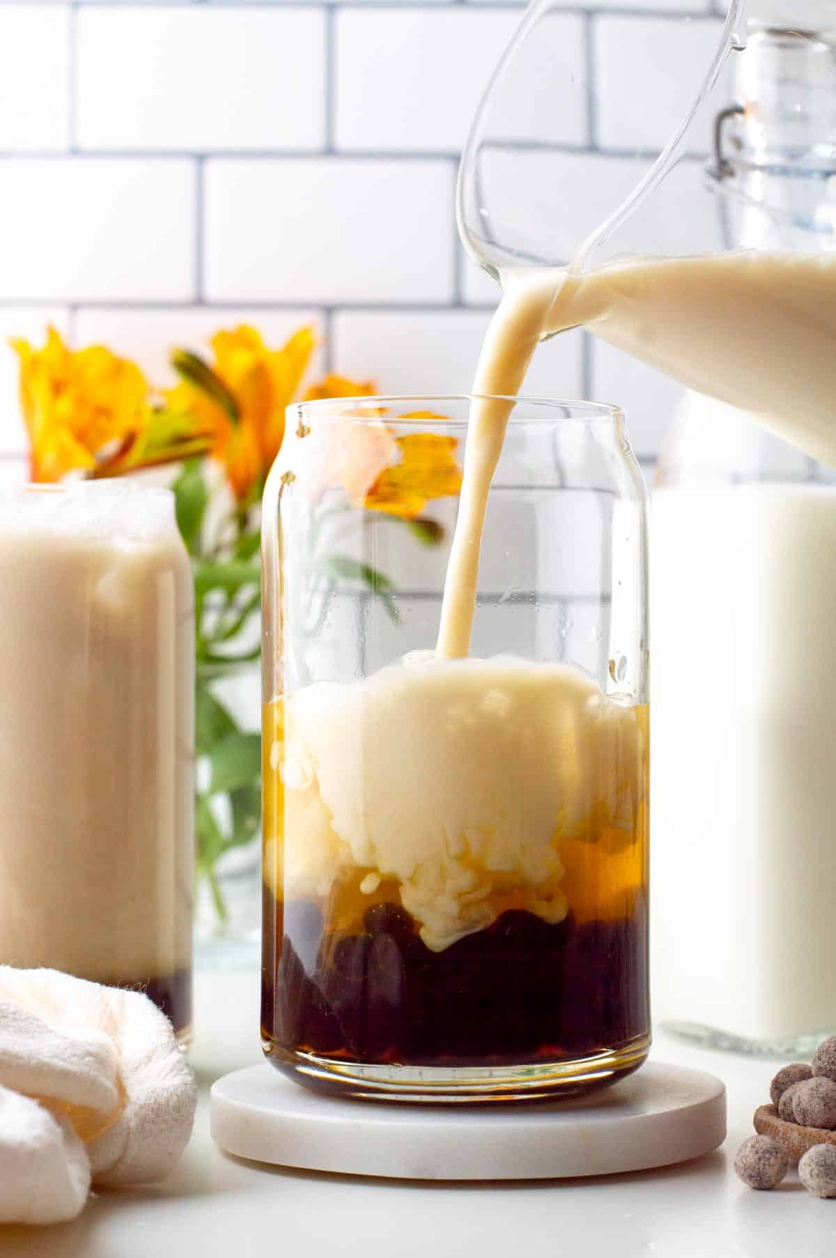 Milk pouring from a pitcher into a glass filled with jasmine tea and boba pearls.