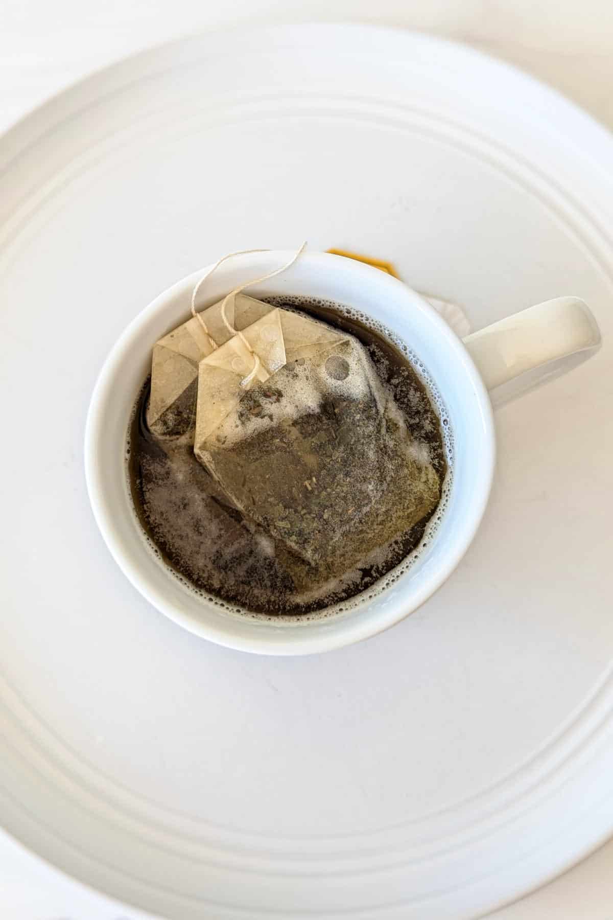 A mug filled with hot water and 2 jasmine tea bags steeping in it.