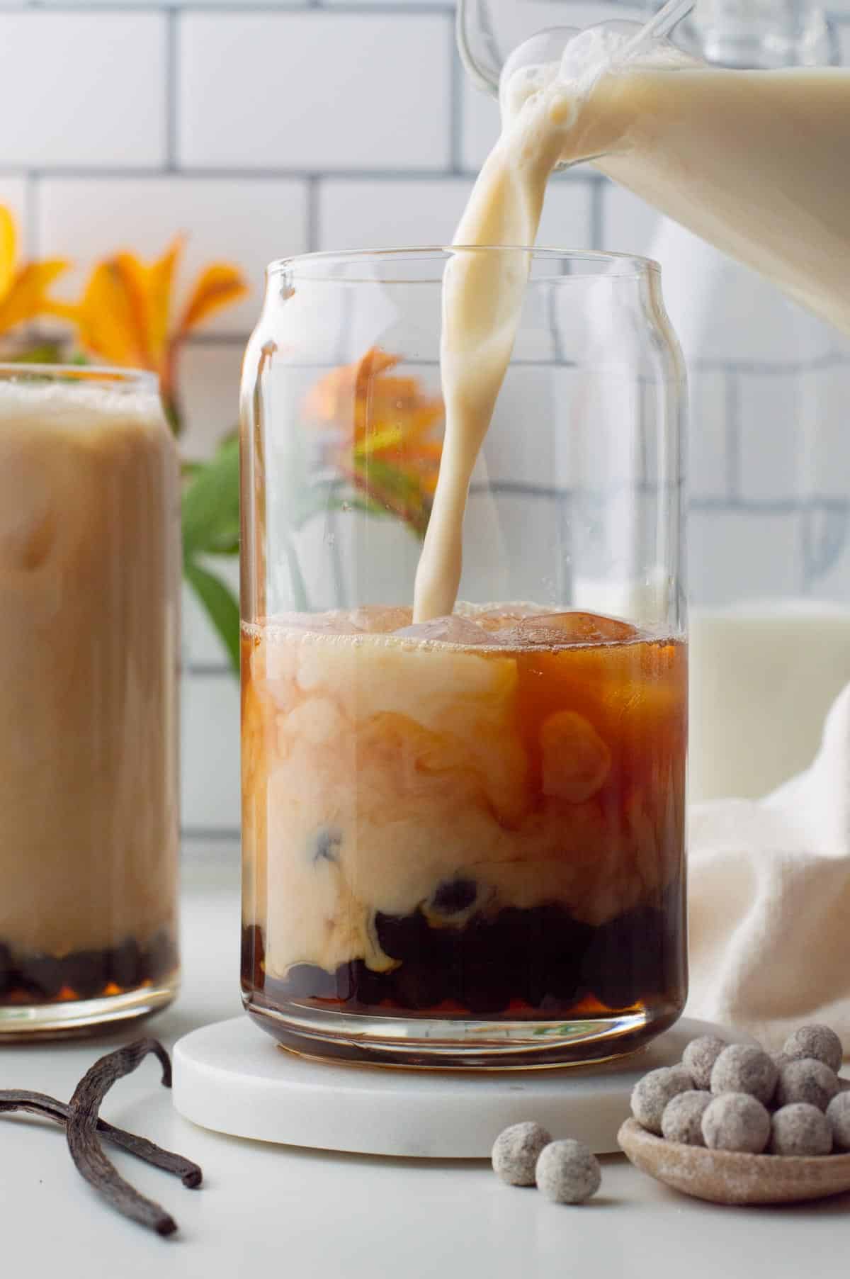 Milk pouring into the glass vanilla tea with boba pearls at the bottom.