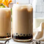 Two glasses of vanilla milk tea with boba pearls in the bottom.