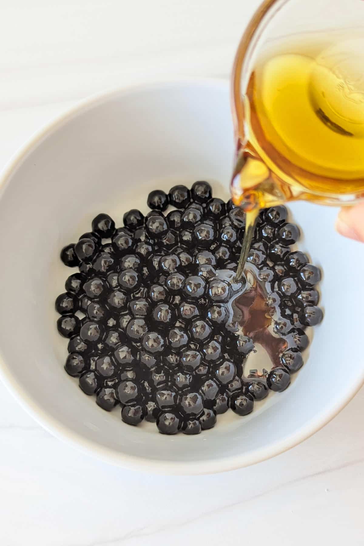 Maple syrup pouring into a bowl of cooked boba pearls.