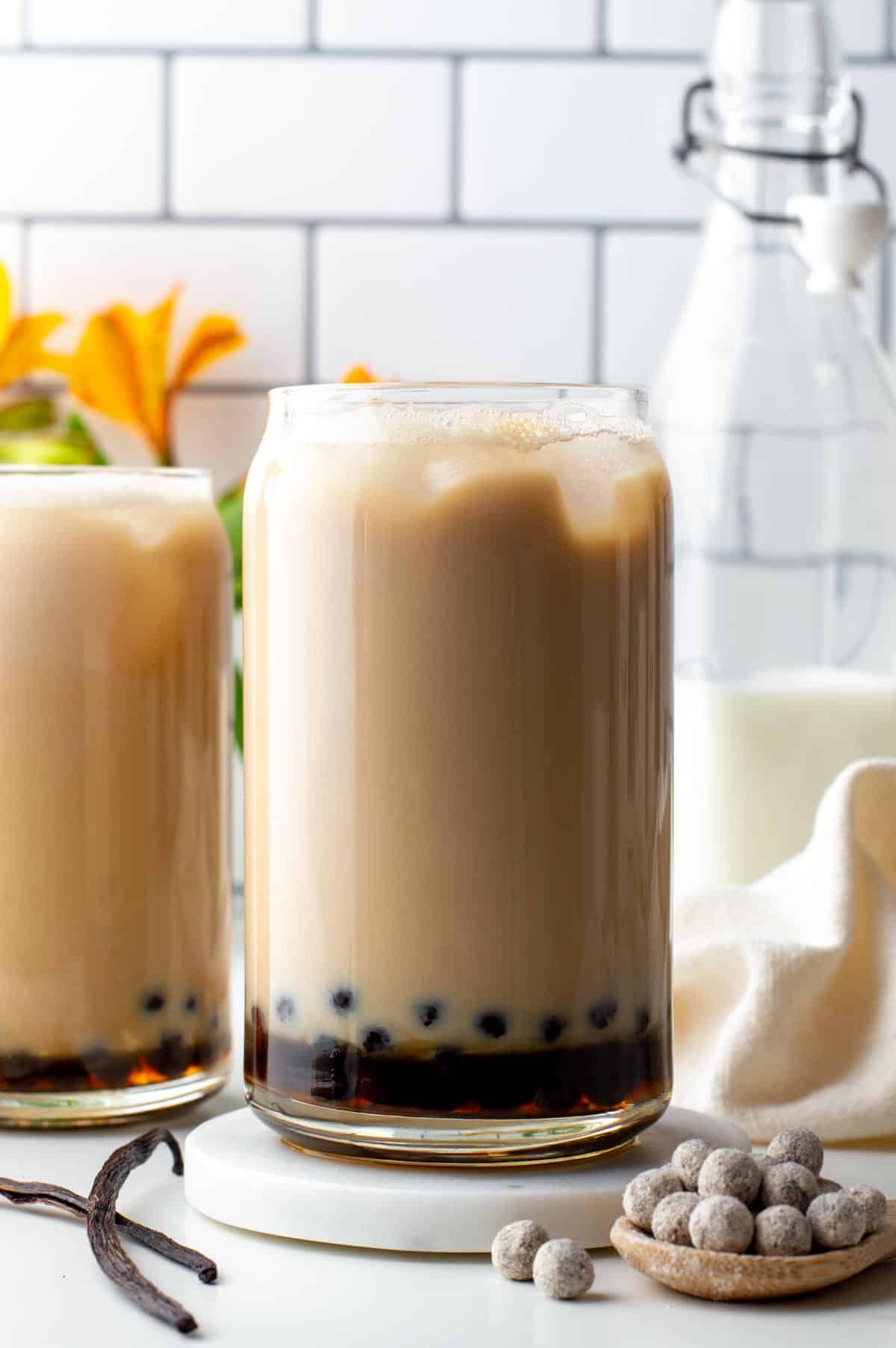 Two glasses of vanilla milk tea with boba pearls in the bottom.