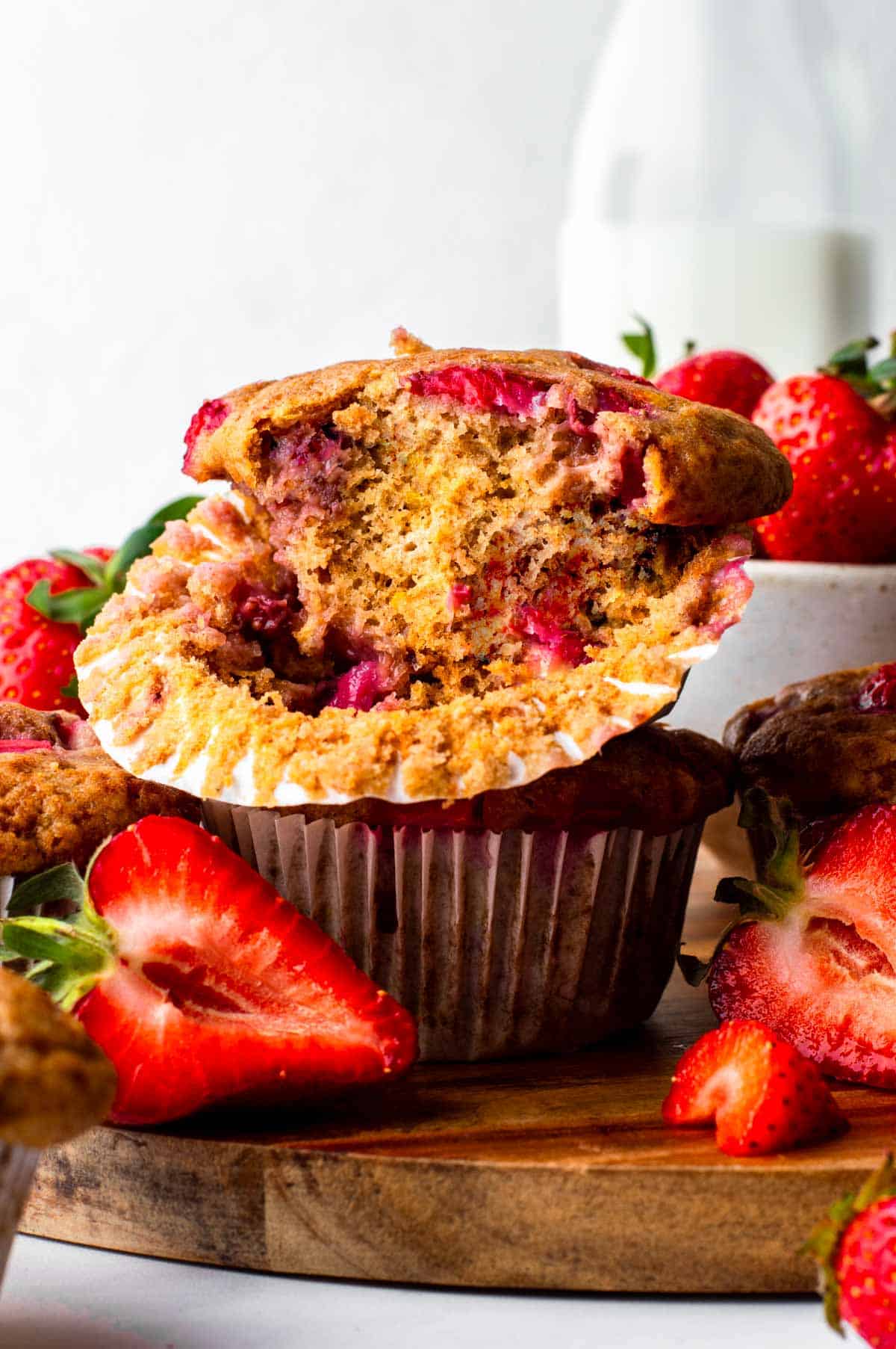 A vegan strawberry muffin stacked on another, with the muffin liner pulled down and a bite taken out to reveal the fluffy inside texture.