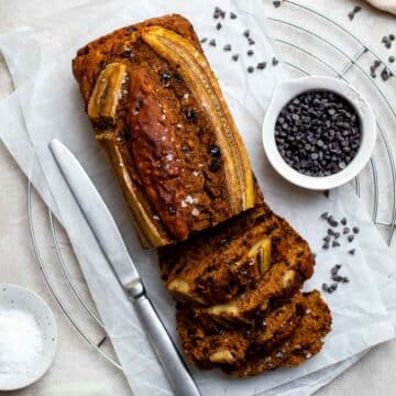 A partially sliced loaf of healthy WFPB banana bread, sprinkled with flaky sea salt.