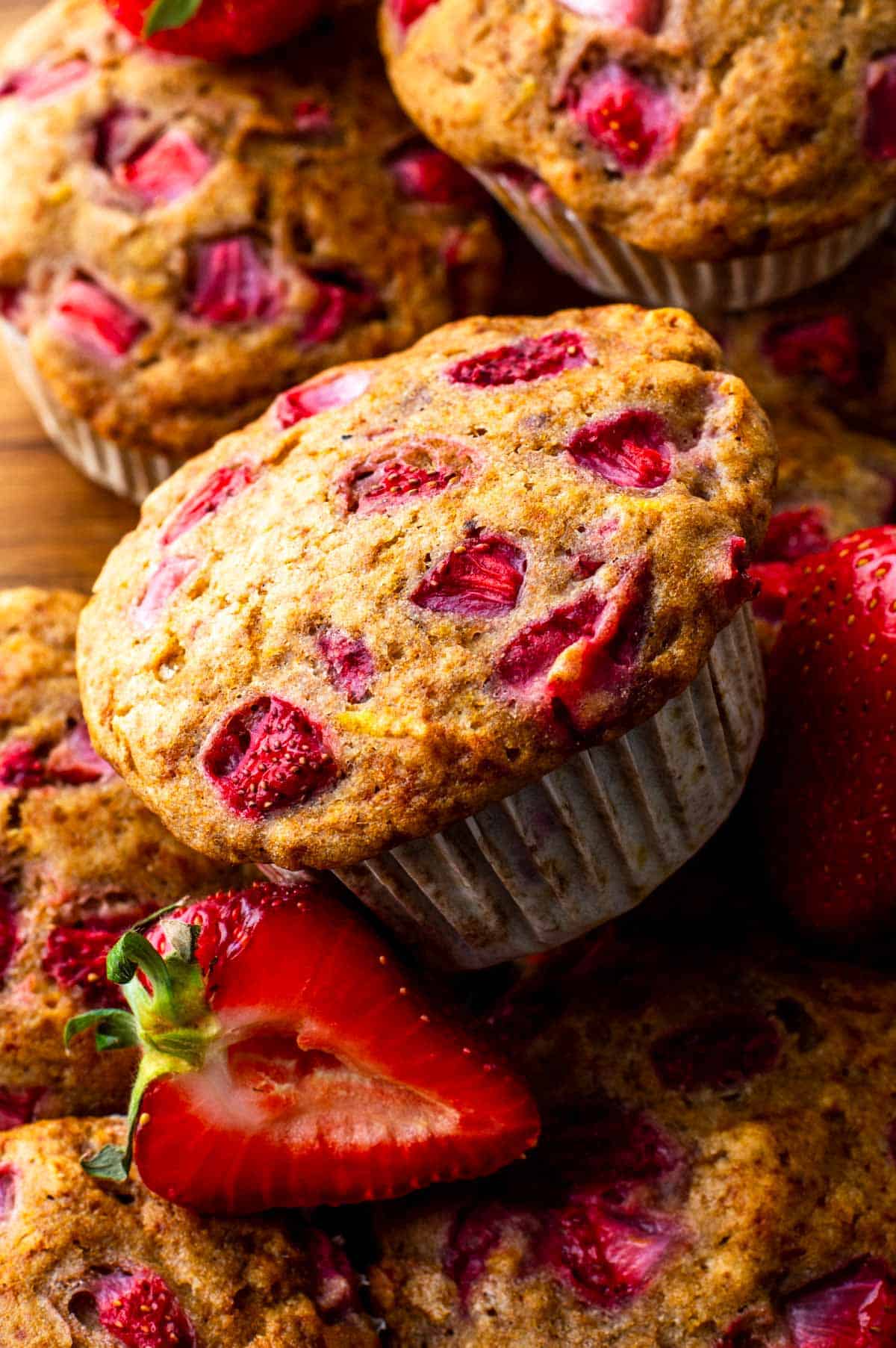 Close-up of a pile of vegan strawberry muffins with golden tops and flecks of strawberries.