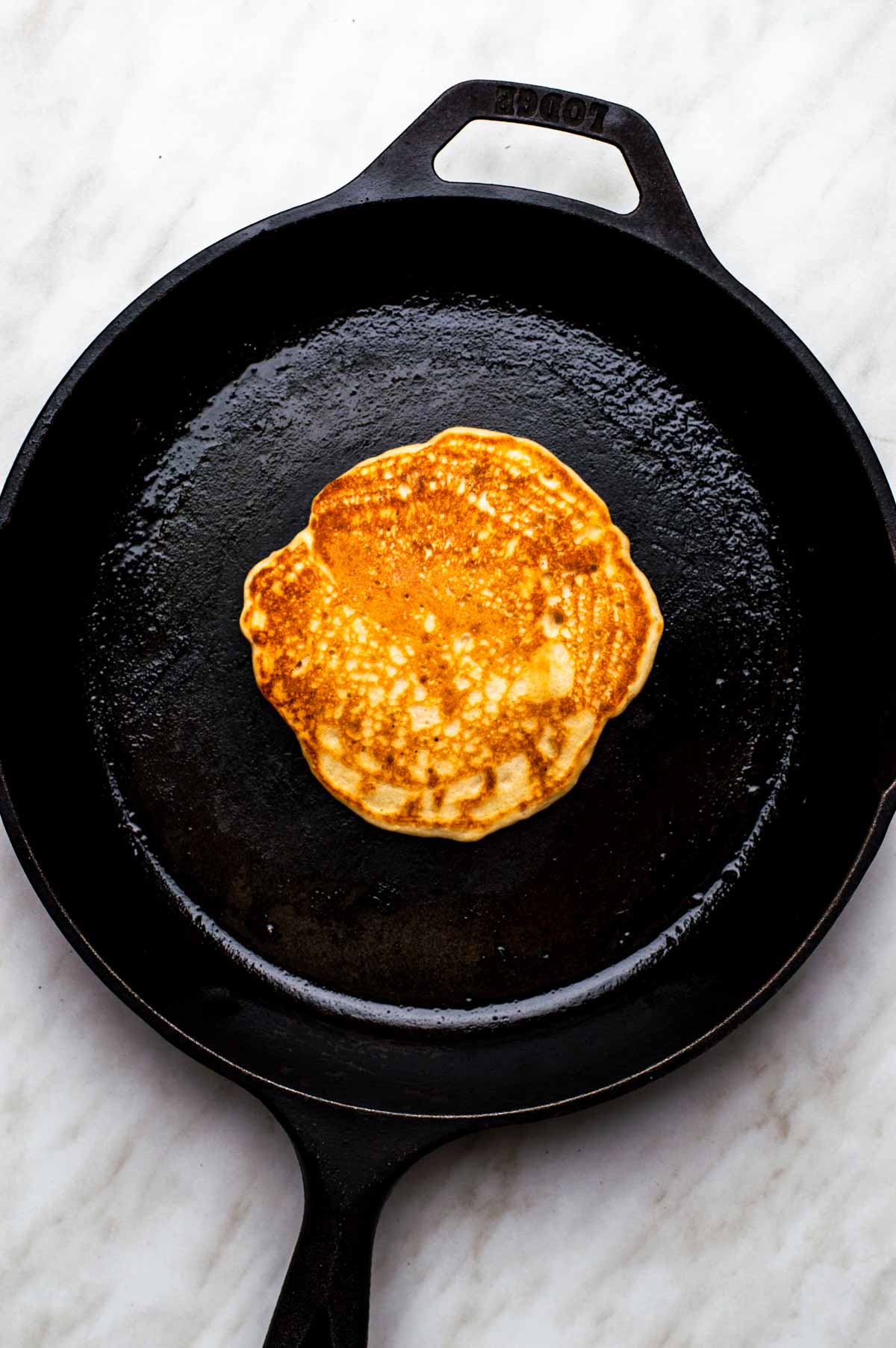 Golden vegan bisquick pancake cooking in a skillet.