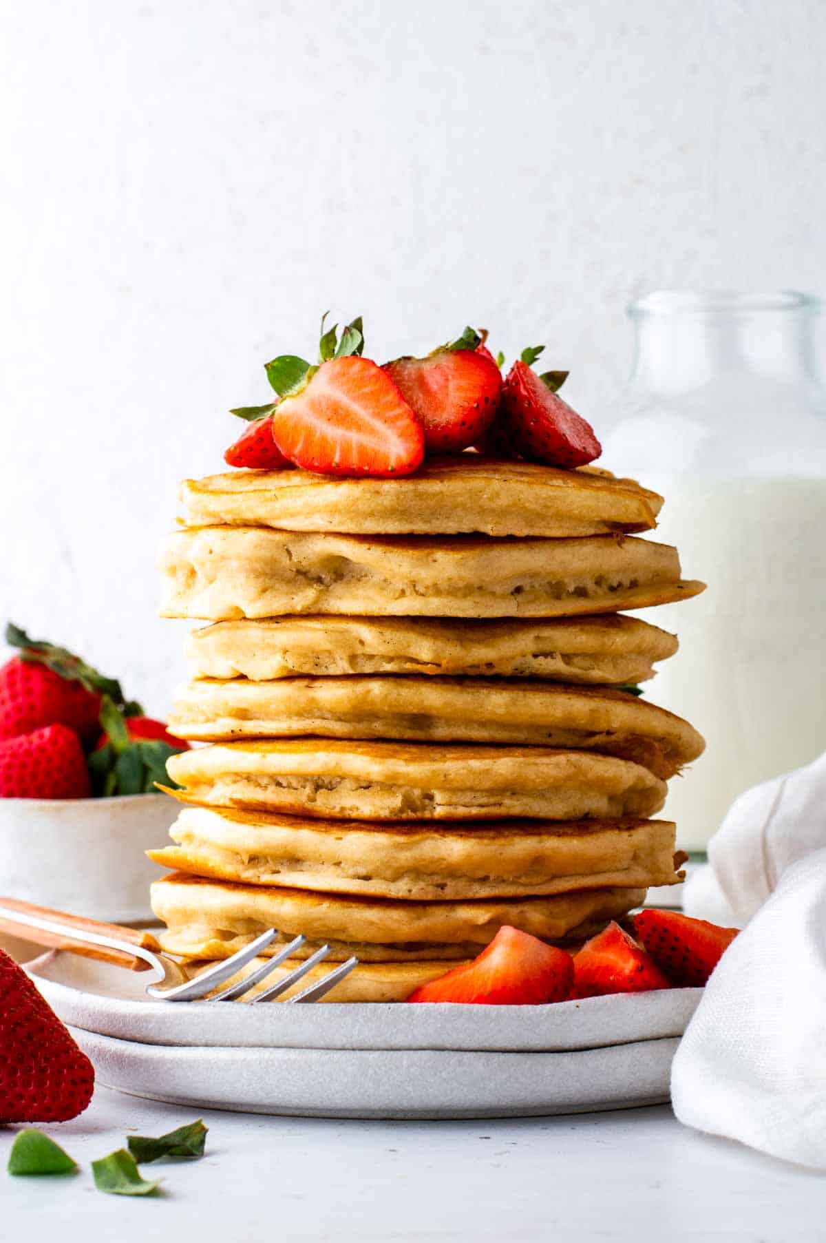 A stack of golden cooked vegan bisquick pancakes sitting on a plate and topped with fresh strawberries.
