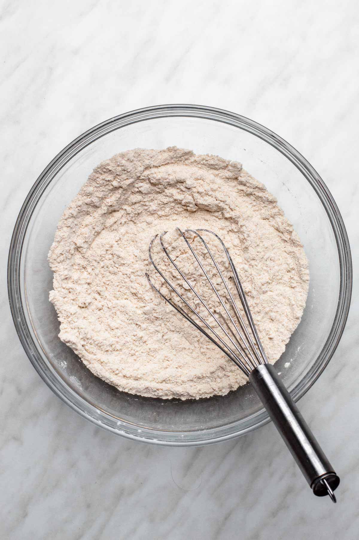 Dry ingredients for vegan strawberry muffins mixed together in a large glass bowl with a whisk.