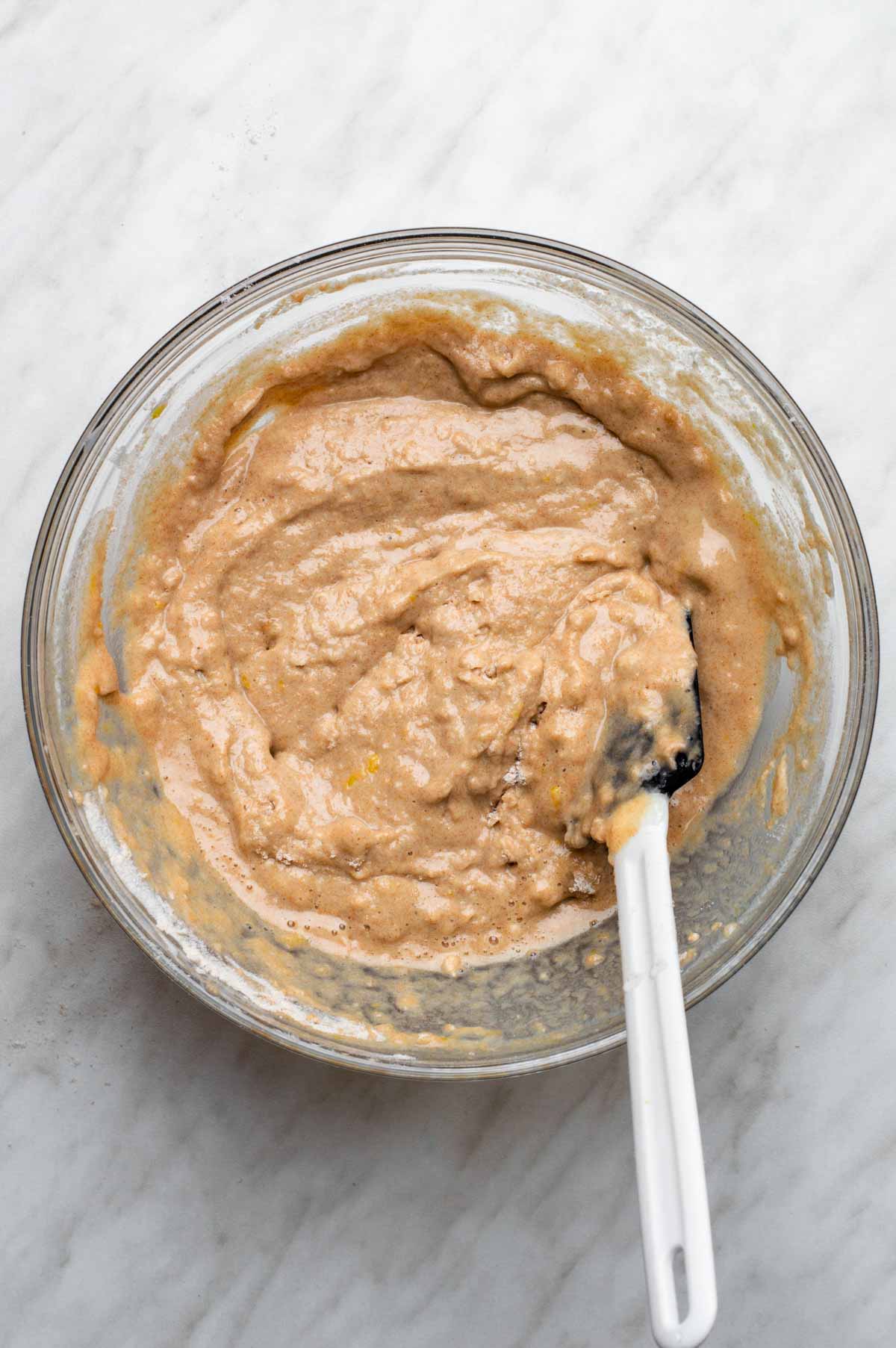 The wet and dry ingredients for vegan strawberry muffins all mixed together to form a batter in a large glass bowl.
