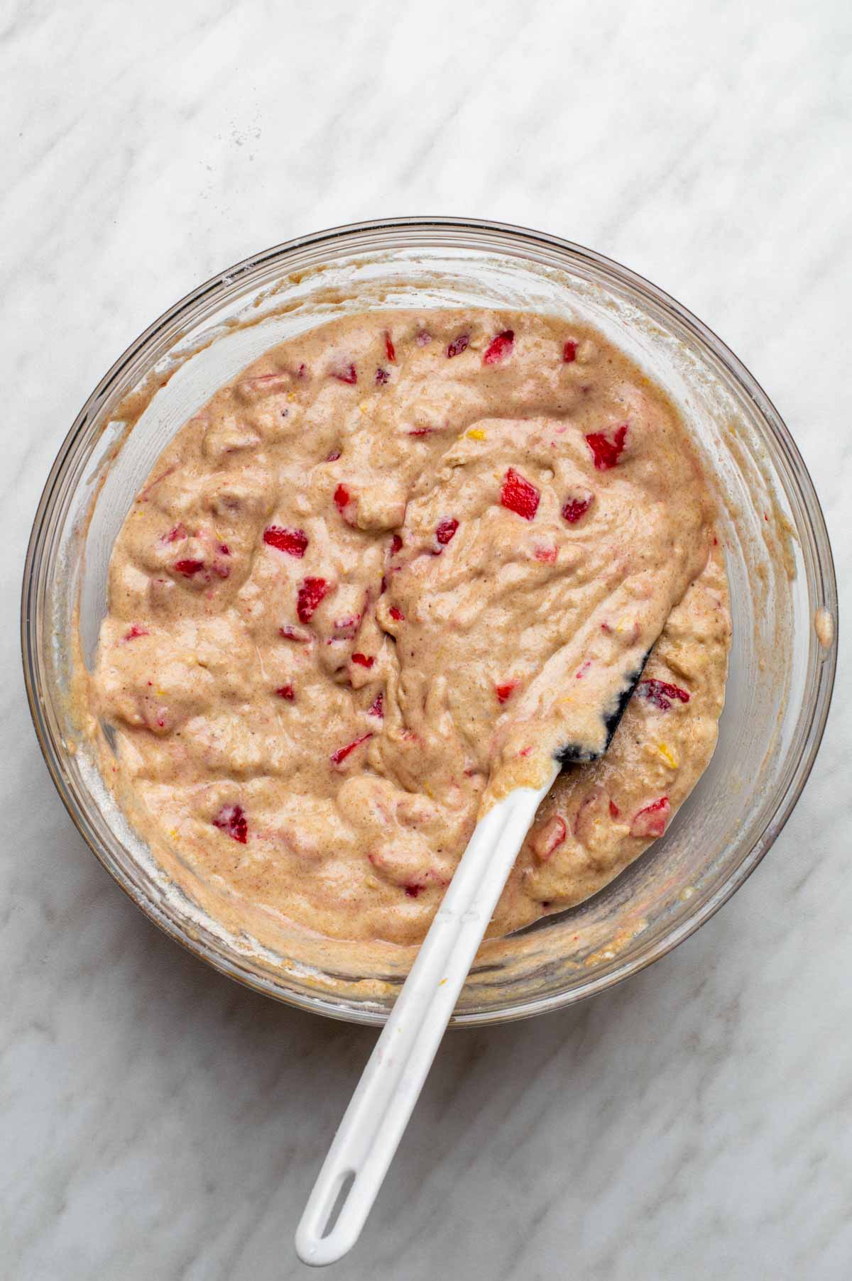 Strawberries evenly dispersed throughout the batter in a large glass mixing bowl.