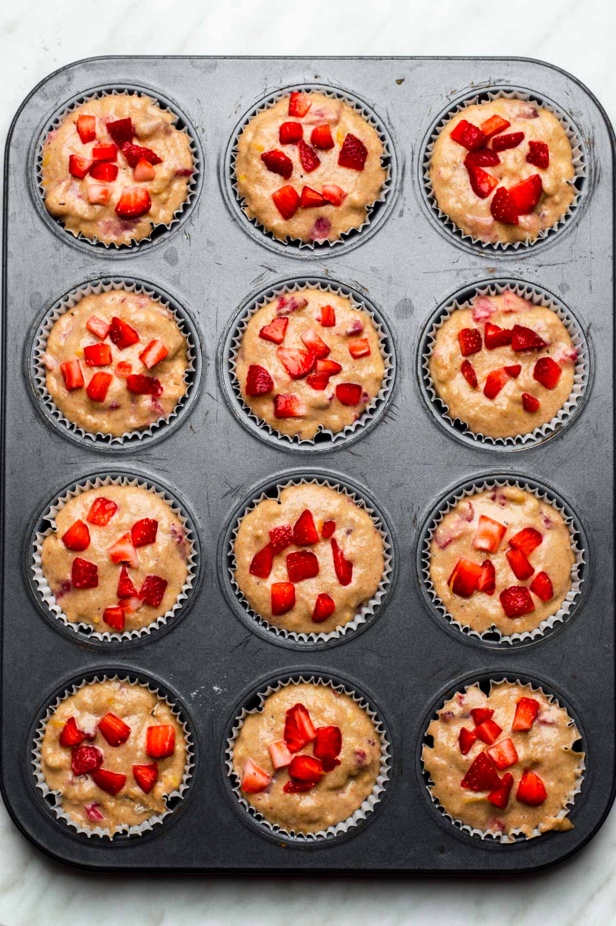 Vegan strawberry muffin batter evenly dispersed into a lined muffin tin.