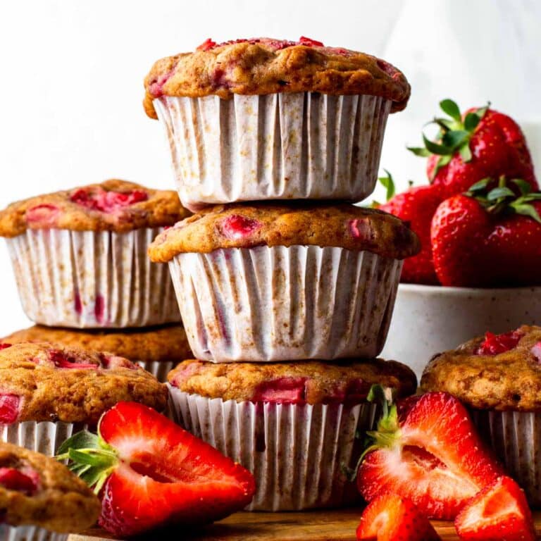 A stack of three vegan strawberry muffins, next to sliced fresh strawberries.