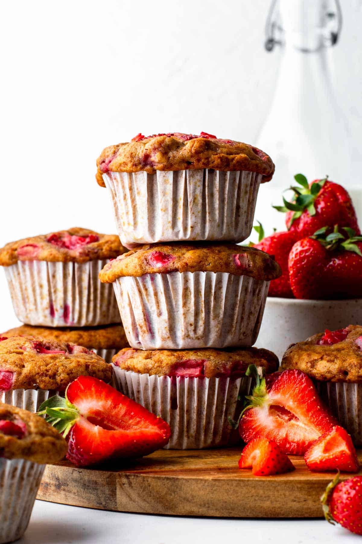 A stack of three vegan strawberry muffins, next to sliced fresh strawberries.