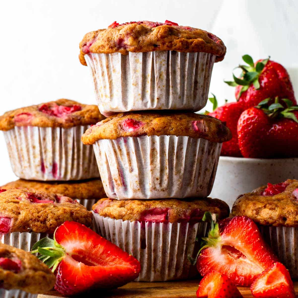 A stack of three vegan strawberry muffins, next to sliced fresh strawberries.